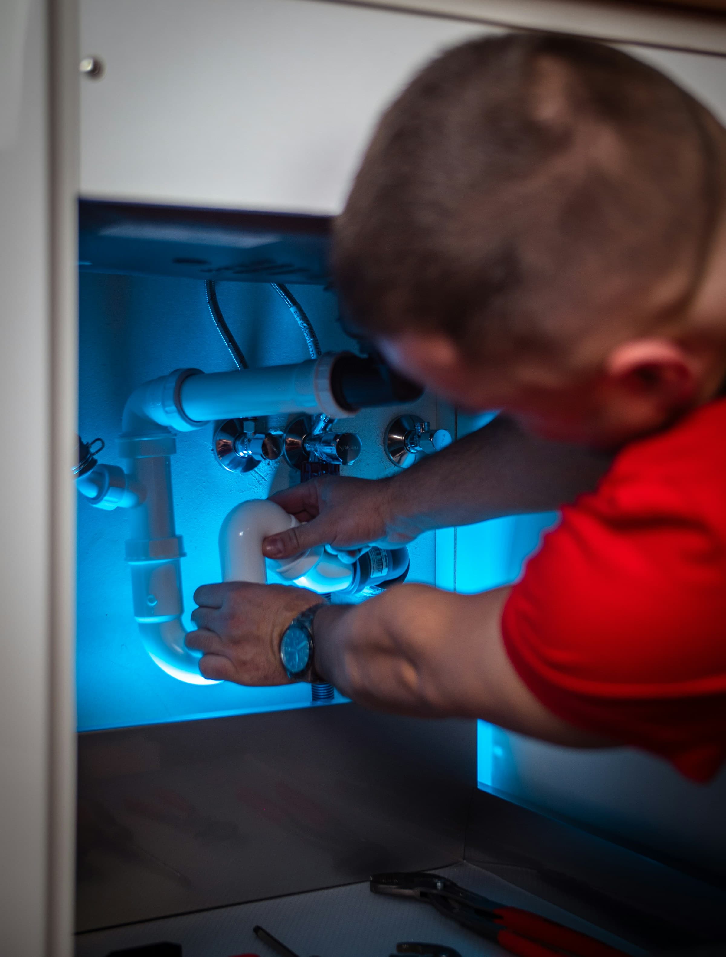 A plumber fitting pipework under a sink